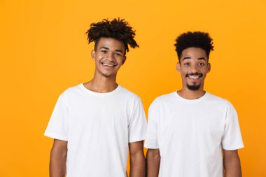 İki mutlu erkek Afrika arkadaşlar sarı arka plan üzerinde izole ayakta t-shirt