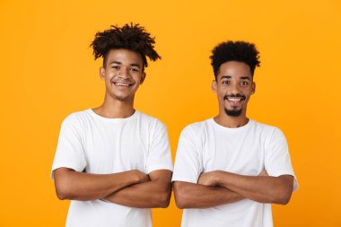 İki mutlu erkek Afrika arkadaşlar sarı arka plan üzerinde izole ayakta t-shirtler katlanmış silah