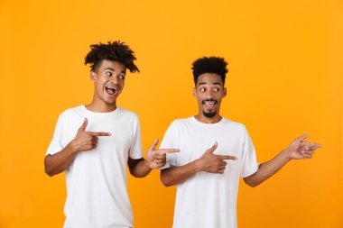Sarı arka plan üzerinde izole ayakta t-shirt uzağa işaret içinde iki neşeli erkek Afrika arkadaşlar