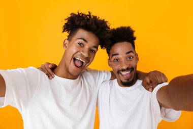 İki sarı arka plan üzerinde izole ayakta t-shirt bir selfie alarak erkek Afrika arkadaşlar heyecanlı
