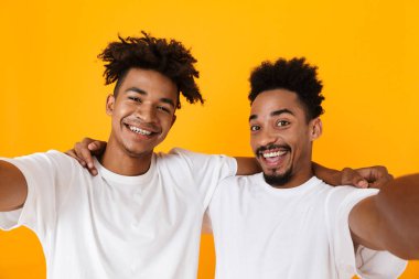 Sarı arka plan üzerinde izole ayakta t-shirt bir selfie alarak iki neşeli erkek Afrika arkadaşlar