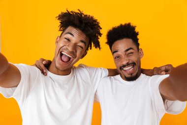 Sarı arka plan üzerinde izole ayakta t-shirt bir selfie alarak iki neşeli erkek Afrika arkadaşlar