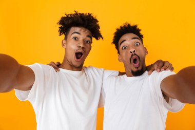 Sarı arka plan üzerinde izole ayakta t-shirt bir selfie alarak iki neşeli erkek Afrika arkadaşlar