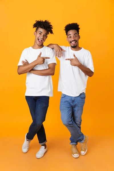 两个快乐的非洲男性朋友的全长在 T恤站立隔绝在黄色背景 指向手指互相 — 图库照片