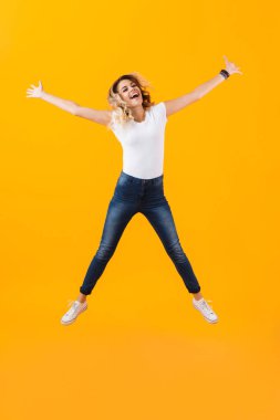 Atlama ve sarı arka plan üzerinde izole gülüyor temel giyim pozitif sarışın kadın fotoğrafı tam uzunlukta