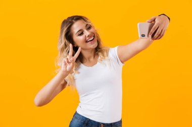 Görüntü gülümseyen ve cep telefonu sarı arka plan izole selfie fotoğrafta çok güzel sarışın kadın