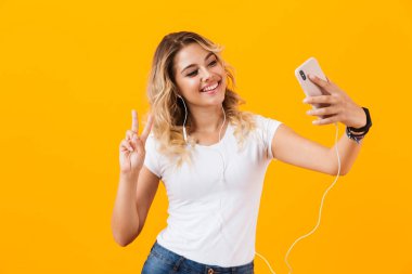 Görüntü gülümseyen ve cep telefonu sarı arka plan izole selfie fotoğrafta kulaklık giyen Avrupa kadın
