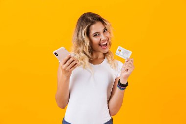Cep telefonu ve kredi kartı üzerinde sarı arka plan izole elinde tutan memnun kadın görüntüsünü