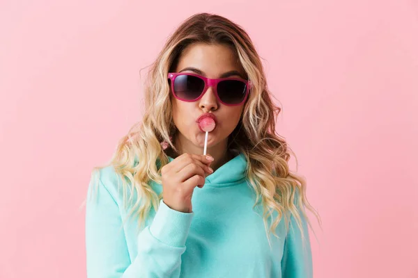 ロリポップ ピンク背景に分離を食べて 代でスタイリッシュな女の子身に着けているサングラスのイメージ — ストック写真