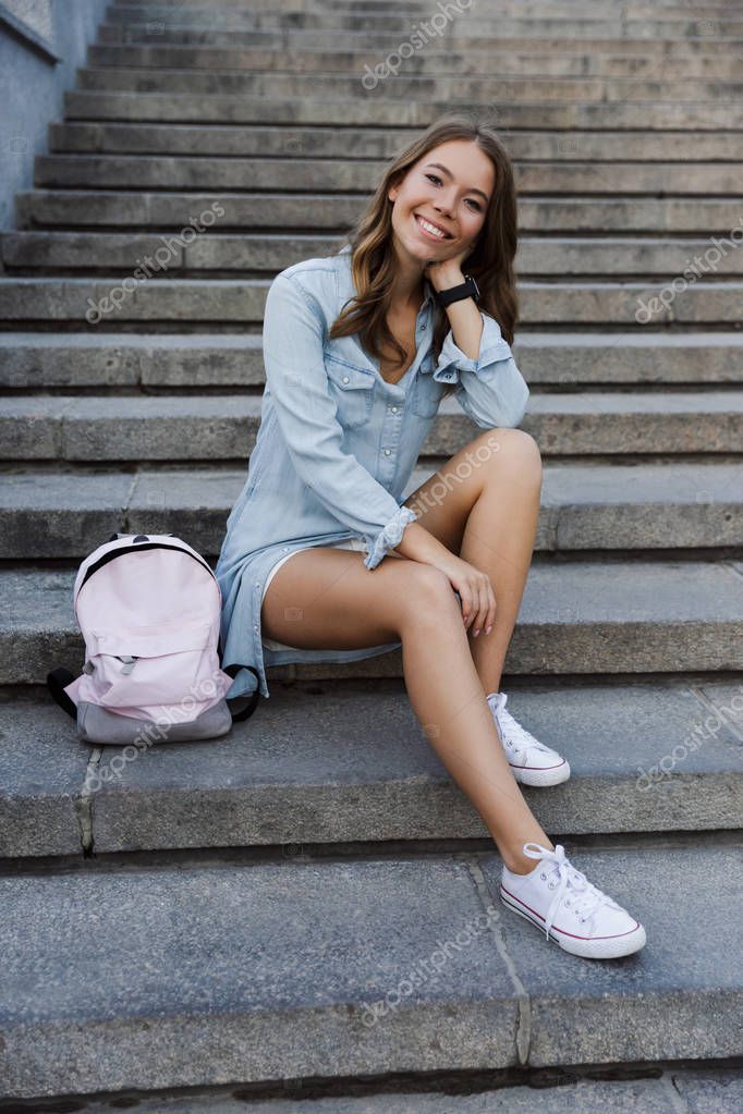 Sonriente joven adolescente con mochila sentado en las escaleras al