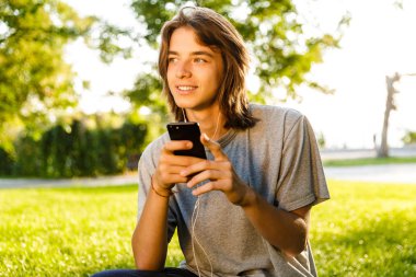Görüntü neşeli genç adam park telefonla sohbet içinde kulaklık ile müzik dinleme.