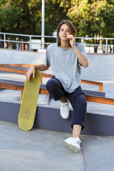 英俊的年轻滑板手坐在公园里的滑板的图像 — 图库照片