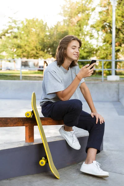 Imagen Joven Patinador Alegre Sentarse Parque Con Monopatín Usando Teléfono —  Fotos de Stock