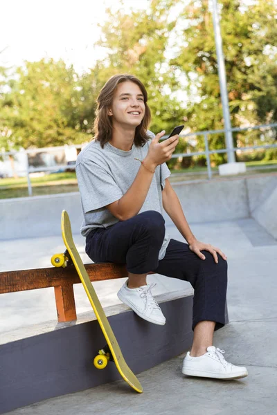 Imagen Joven Patinador Alegre Sentarse Parque Con Monopatín Usando Teléfono — Foto de Stock