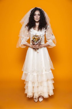 Ölü Gelin zombie Halloween korkunç makyaj çiçekler izole sarı arka plan üzerinde tutarak ve gelinlik giyen tam boy görüntü