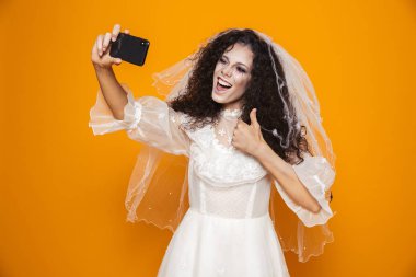 Neşeli gelin zombie Halloween gelinlik ve cep telefonu sarı arka plan izole selfie alarak korkunç makyaj giyen görüntüsünü