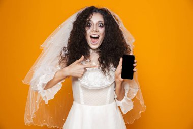 Cep telefonu sarı arka plan izole kullanarak düğün elbise ve tatil makyaj Halloween heyecanlı zombi kadın görüntüsünü
