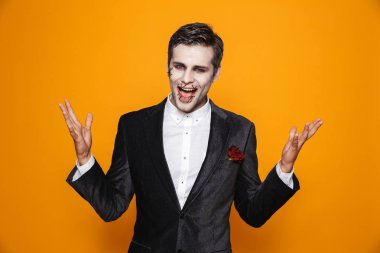 Sarı arka plan üzerinde izole kamera bakarak Damat takım elbise ve Cadılar Bayramı makyaj heyecanlı zombi adam fotoğrafı