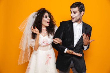 Mutlu zombi çift damat ve gelin düğün kıyafeti ve Cadılar Bayramı makyaj sarı arka plan üzerinde izole gülen fotoğrafı