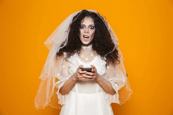恐怖僵尸妇女的图像在万圣节穿着婚纱和节日化妆使用手机孤立在黄色背景 — 图库照片