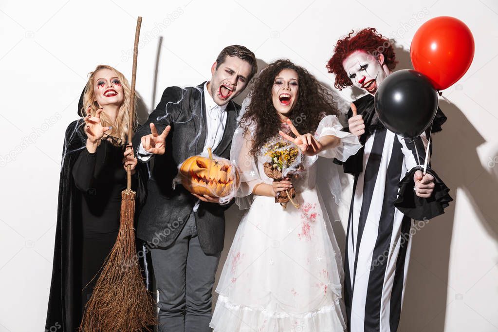 Group of friends dressed in scary costumes celebrating Halloween isolated over white background, holding balloons, curved pumpkin, broom