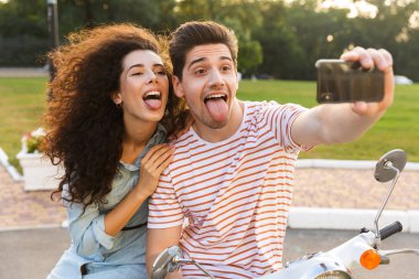 Şık çift erkek ve kadın selfie birlikte şehir parkı içinde motosiklet üzerinde otururken cep telefonu alarak fotoğraf
