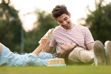 Mutlu çift erkek ve kadın 20'li yaşlarda görüntü park ve okuma kitabı yeşil çim üzerinde yalan
