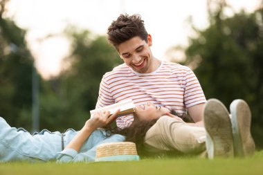 Görüntü neşeli çift erkek ve kadın 20'li yaşlarda park ve okuma kitabı yeşil çim üzerinde yalan