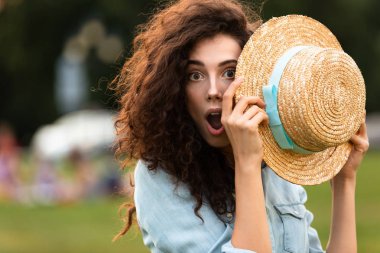 Görüntü arka plan bulanık ile yeşil parkta yürürken sürpriz kadın 20'li yaşlarda holding hasır şapka