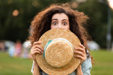 Yeşil parkta yürürken hasır şapka ile heyecanlı kadın 20'li yaşlarda kapsayan yüz görüntü