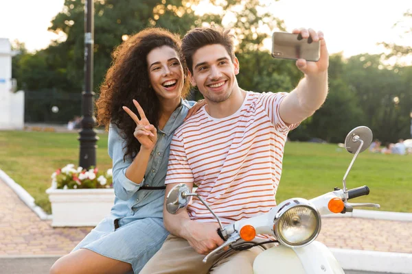 きれいなカップル男女都市公園におけるバイクで一緒に座って携帯電話で Selfie を撮影の写真 — ストック写真