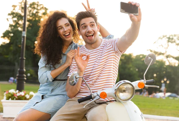 图为浪漫夫妇在城市公园一起坐在摩托车上 拿着手机自拍 — 图库照片