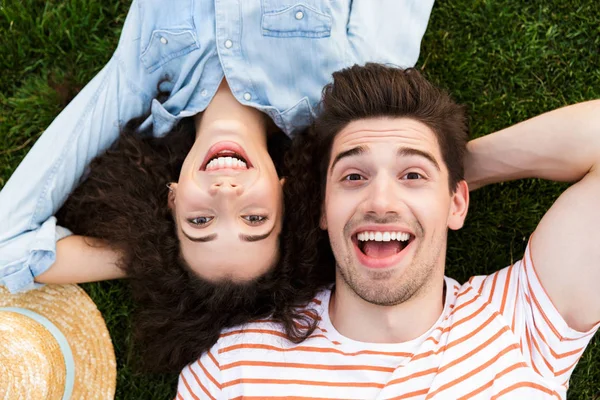 Görüntü neşeli çift erkek ve kadın 20'li yaşlarda üstten Park yeşil çimenlerin üzerinde ters kafa yanında yalan