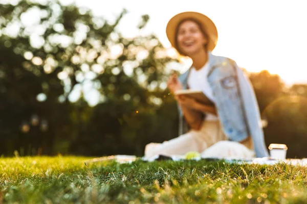 ぼやけて表示ノートに書く公園で芝生の上に座っている若い女の子を笑いながら — ストック写真