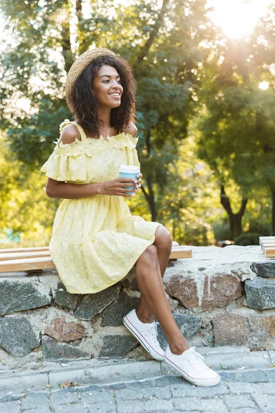매력적인 모자와 공원에서 벤치에 앉아와 테이크 커피를 마시는 드레스 — 스톡 사진