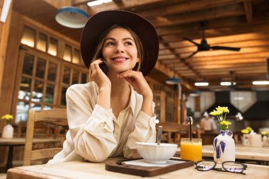 Rahat kafede otururken Smartphone'da konuşan şapka giyen beyaz kadın portresi