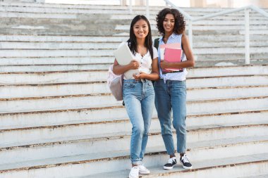 Açık havada duran, kitap tutan iki mutlu genç öğrenciler kız tam uzunlukta