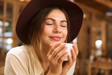 Holding fincan çay kapalı, kafeterya masada oturan şapkalı gülümseyen bir kızın yakın çekim