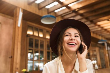 Kapalı, kafeterya masada oturan şapkalı bir gülen kız cep telefonu üzerinde konuşurken, yakın çekim