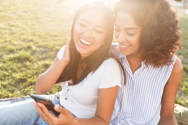 Två Glada Unga Studenter Flickor Sitter Gräs Utomhus Innehav Mobiltelefon — Stockfoto