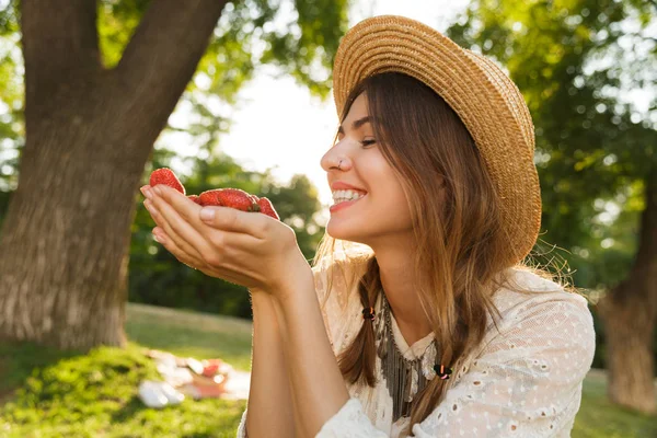 关闭可爱的年轻女孩在夏天帽子花时间在公园 举行草莓堆 — 图库照片