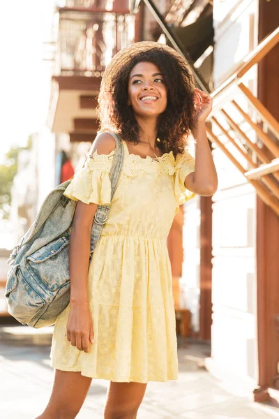 Neşeli Afrikalı-Amerikalı kadın 20'li yaşlarda giyen hasır şapka ve elbise yürüyüş güneşli gün boyunca açık boy fotoğrafı