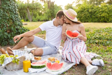 Birlikte iyi vakit, parkta piknik, öpüşme genç çift gülümseyen