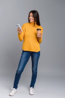 Paket servisi olan restoran kahve cep telefonuyla tutan gri arka plan üzerinde izole bir rahat genç kadın portresi tam uzunlukta