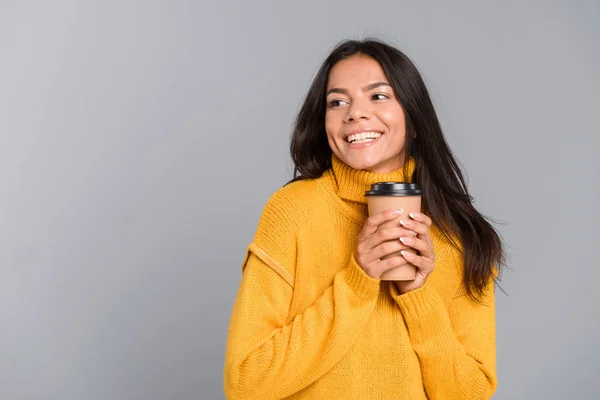 一个面带微笑的年轻女子拿着外卖咖啡杯的肖像 隔着灰色的背景 望着一边 — 图库照片