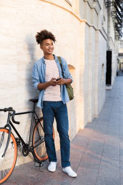 Bisiklet ile açık havada cep telefonuyla sokakta dolaşan genç Afrika adam fotoğrafı.