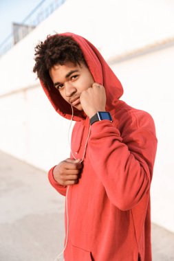 Kulaklık ile müzik dinlemek hoodie ayakta plajda giymiş kendine güvenen genç Afrika genç bir yakın çekim