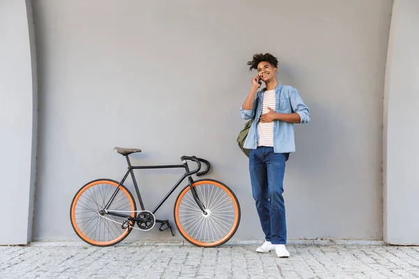 自転車携帯電話で話していると屋外で歩く幸せな若いアフリカ男のイメージ — ストック写真