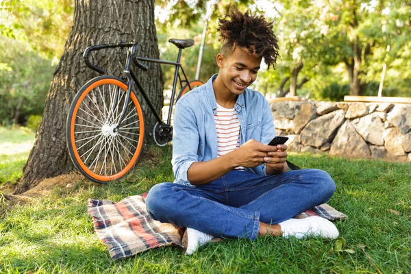 Cheerful Young African Teenager Backpack Outdoors Sitting Grass Using Mobile — Stock Photo, Image