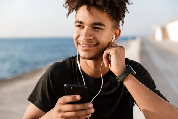 一个年轻人运动员走在户外的海滩上听音乐与耳机的图像 — 图库照片